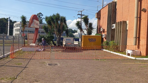 Foto externa do pátio da ESP, com o prédio da escola em tijolo à vista à direita e o canteiro de obras à frente, com um homem caminhando. Ao fundo se vê a Avenida Ipiranga.