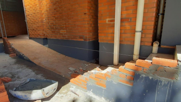 Em um prédio de tijolos à vista, vê-se uma escada de cinco degraus que está sendo reformada com novos tijolos.