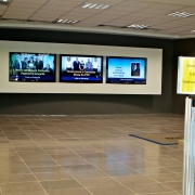Saguão de entrada da Procergs, com 3 telas exibindo notícias da empresa ao lado de escadaria principal