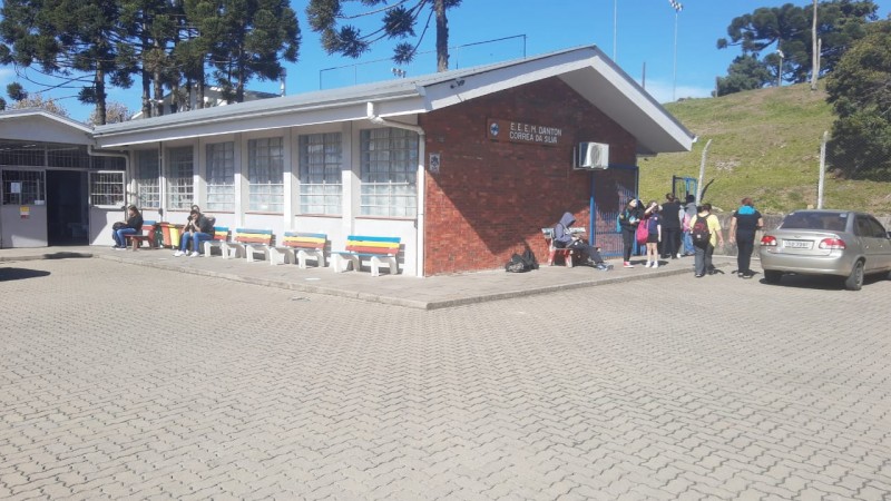 O prédio da escola Danton Correa da Silva com alunos em sua volta e um carro estacionado à direita.