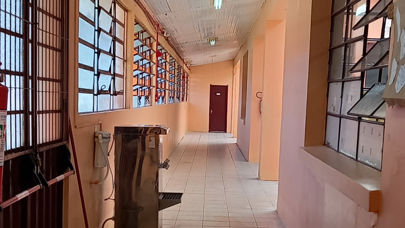 Corredor de escola com saída de emergência e bebedouro à esquerda.