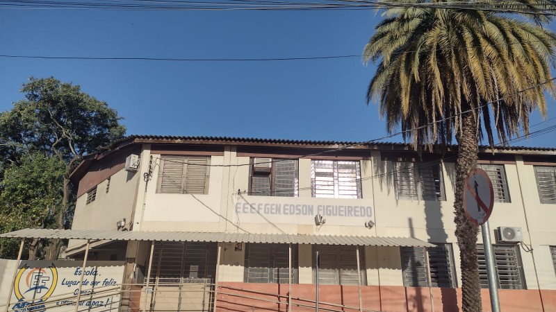 Fachada da escola General Edson Figueiredo com uma palmeira e uma placa de trânsito à frente.