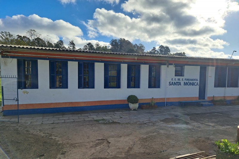 Prédio com letreiro com nome da escola, pintado em branco com faixas laranja e azul.
