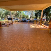 Entrada da escola, vista da parte interna, com um banco à direita e corrimãos à frente, tendo ao fundo uma casa e carros estacionados.
