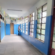 Em um corredor de escola, uma mulher olha por uma das janelas.
