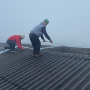 Em meio à névoa, dois homens puxam um fio de ferro sobre o telhado da escola.