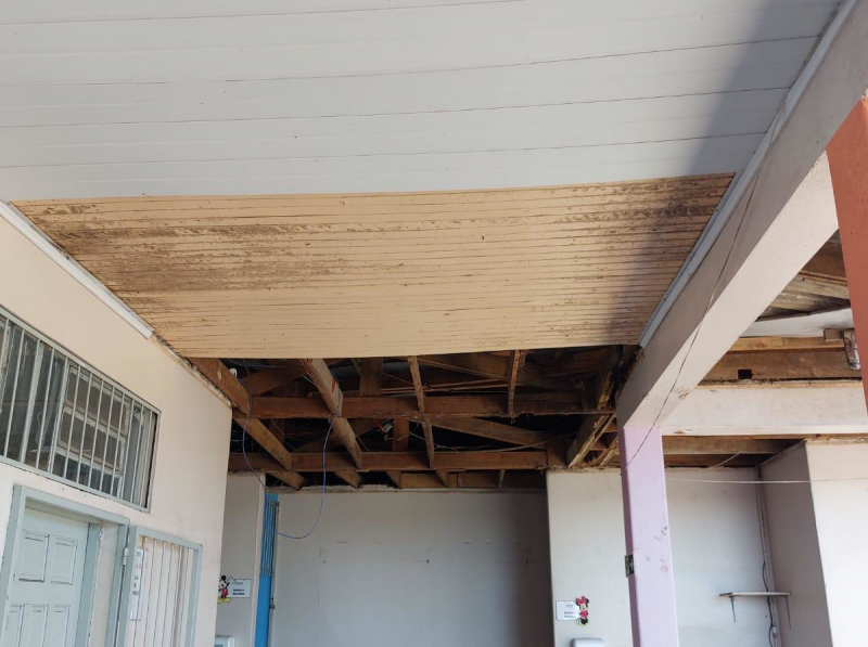 Foto da cobertura do corredor interno da escola, com parte em pintura branca, outra com pintura amarelada e suja e parte sem cobertura, com madeirame à mostra.
