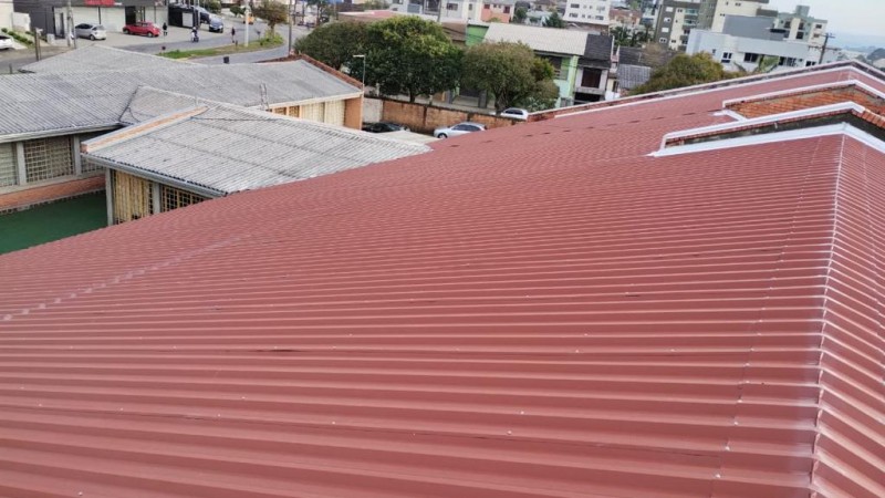 Em primeiro plano, o telhado vermelho da escola. Ao fundo se vê parte do prédio da escola e casas da cidade.