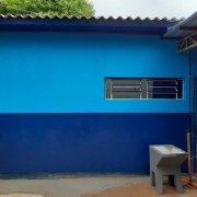 Prédio de escola em dois tons de azul, com pia à frente e grade azul ao lado.