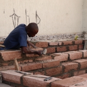 Homem trabalha em obra assentando pedras com cimento.