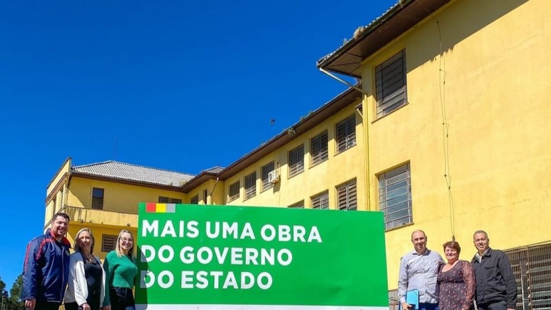 Em frente ao prédio de três andares pintado de amarelo, três homens e três mulheres posam nos lados da placa verde que anuncia o investimento do governo do Estado.