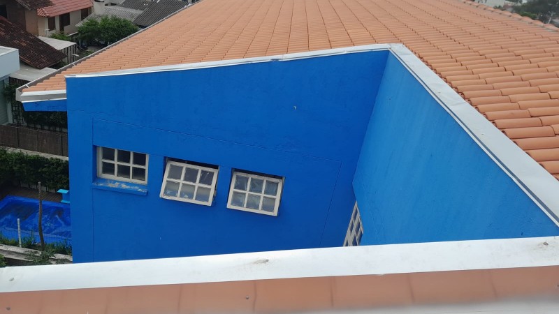 Vista do telhado do prédio da escola, com telhas cor de argila e prédio na cor azul.