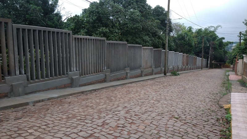 Rua de calçamento de pedra com muro pré-moldado à esquerda.