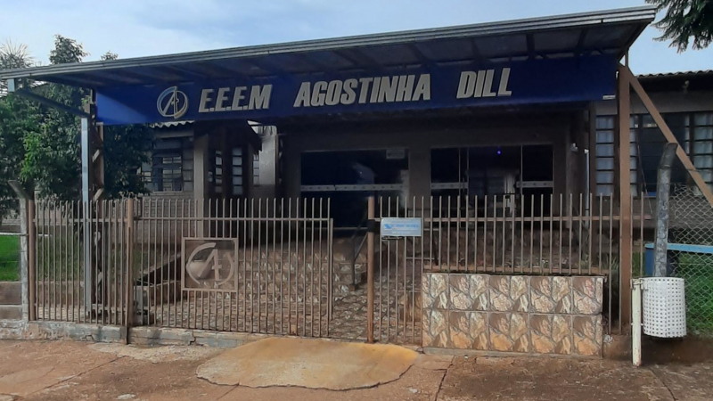 Vista da entrada da escola, um prédio de um andar. A entrada é uma área coberta com um letreiro azul com o nome e o logo da escola.