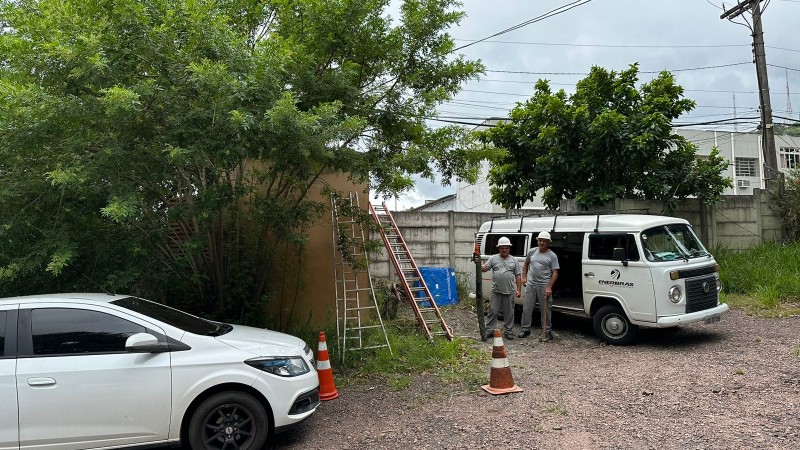 Vê-se um carro e uma Kombi brancos, dois homens e três escadas.