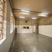 Parte interna do bloco do refeitório, com janelas à esquerda e a cozinha ao fundo.