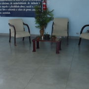 Em uma sala de paredes azuis, vê-se ao centro três cadeiras e uma mesa enfeitada, uma planta e dois quadros de avisos azuis. À esquerda, uma porta aberta dando para o pátio da escola.
