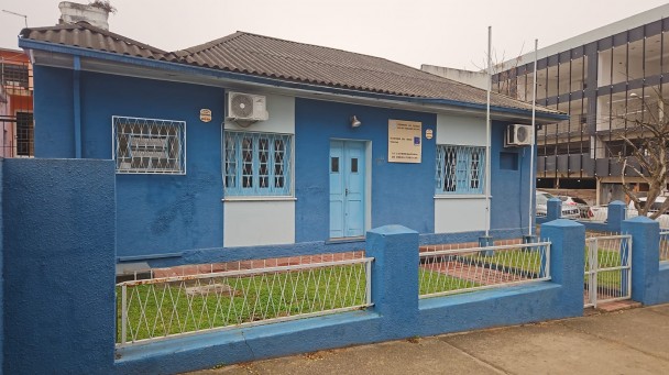 Imagem de uma casa pintada em azul e cinza. À direita, se vê um prédio em construção.