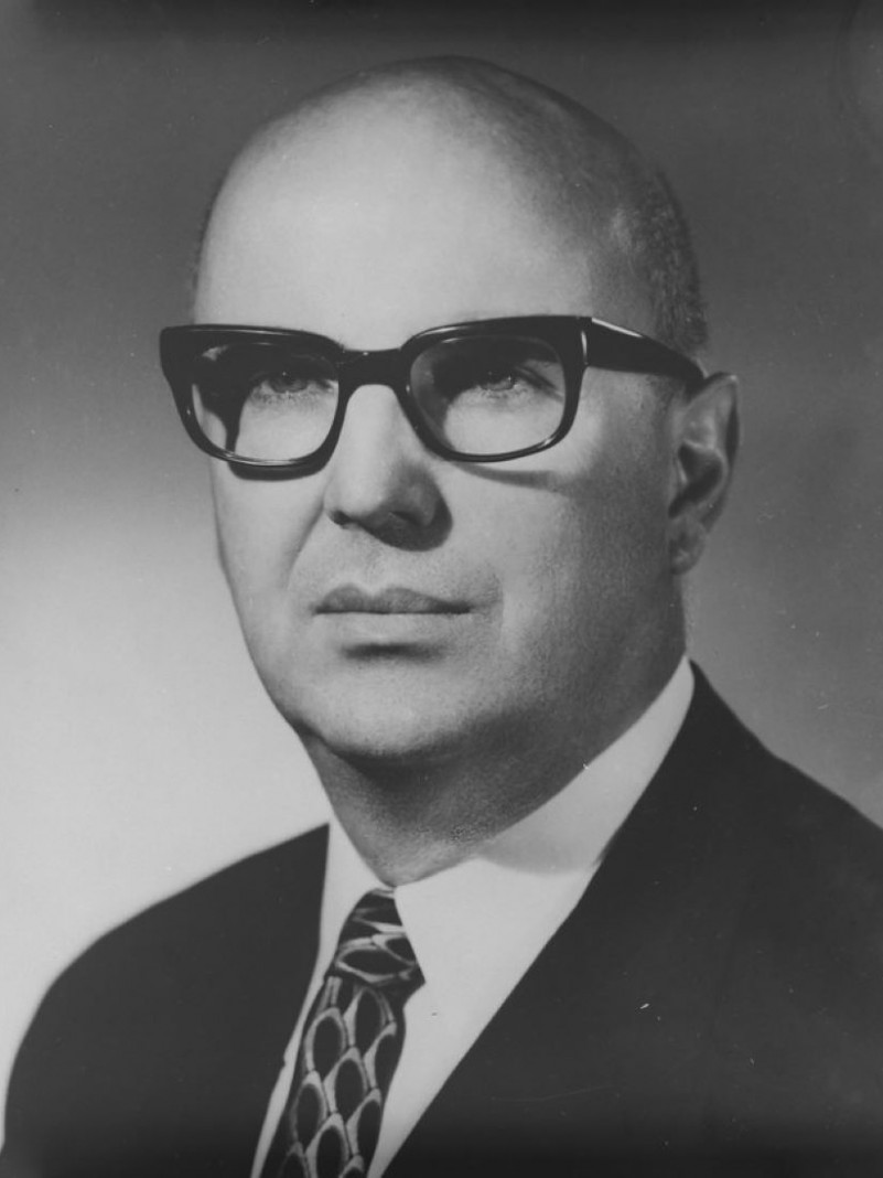 Foto em preto e branco de um homem branco, careca, de &oacute;culos de arma&ccedil;&atilde;o grossa preta, vestindo terno e gravata.