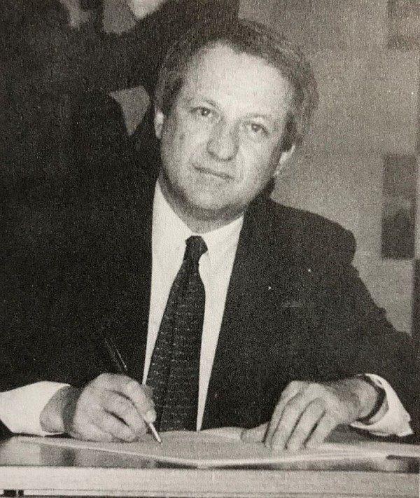 Foto de um homem branco vestindo terno e gravata assinando a Constituição de 1988.