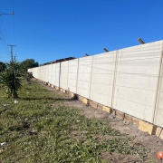 Foto de um muro de concreto pré-moldado. À esquerda, grama e arbustos.