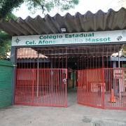 Foto da fachada da escola. Envolto por muros verdes, vê-se o portão vermelho da escola, encimado pelo letreiro com o nome da instituição.