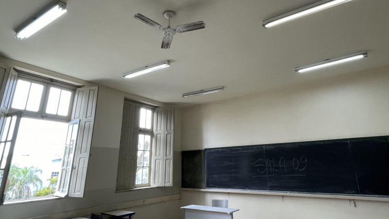 Foto interna de uma sala de aula vazia com as janelas abertas.