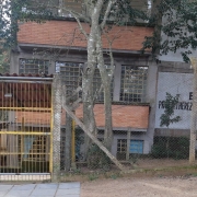 Foto da fachada da escola. O prédio tem três pisos e há árvores na frente da escola.