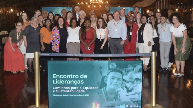 Um grupo de pessoas posa atrás de uma TV onde se lê "Encontro de lideranças", com uma foto de criança.