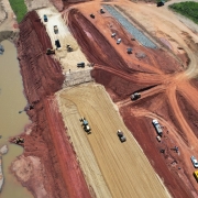 Foto aérea da construção da barragem com patrolas trabalhando.