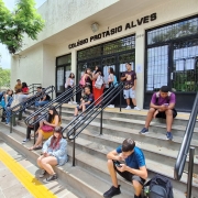 Foto da frente do Colégio Protásio Alves. Na escadaria, jovens sentam ou se reúnem em grupos.