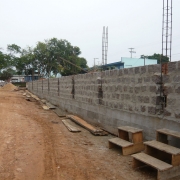 Foto de um muro em construção ao lado de uma rua de chão batido.