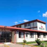 Foto da fachada da escola, pintada em branco e vermelho. O céu está azul.