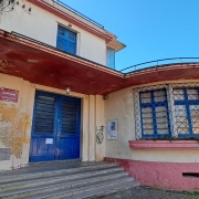    Foto da fachada de uma escola, um prédio de dois pisos pintado em tons de bege.