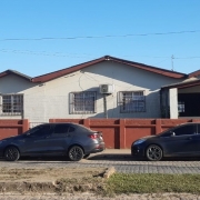 Foto de uma escola, de um piso, com carros estacionados à frente deles.