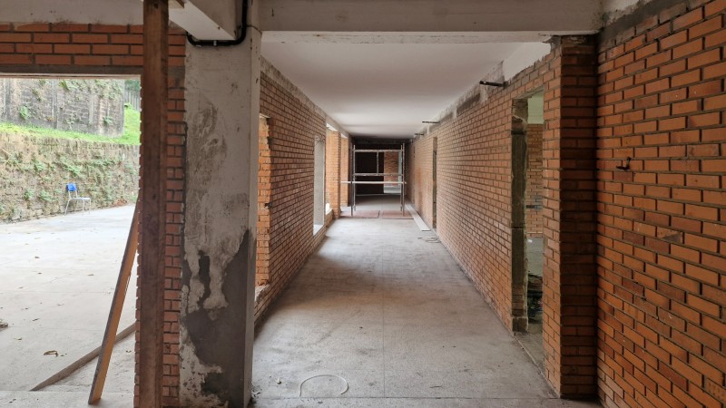    Foto de um corredor de escola, em tijolo à vista, passando por obras.
