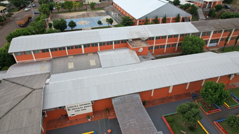 Foto aérea dos prédios de uma escola, em tijolo à vista, com o ginásio e a quadra de esportes ao fundo.