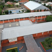 Foto aérea dos prédios de uma escola, em tijolo à vista, com o ginásio e a quadra de esportes ao fundo.