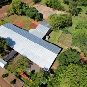 Foto aérea que mostra o telhado da escola, a quadra descoberta de esportes, a área verde com árvores e a rua.