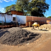 Tirada da rua, onde há pedra brita e areia empilhadas, além de uma betoneira, vê-se o muro em reconstrução.