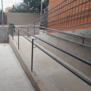 Foto do espaço entre dois prédios da escola, onde se vê uma rampa de acesso. Os prédios são em tijolo à vista.