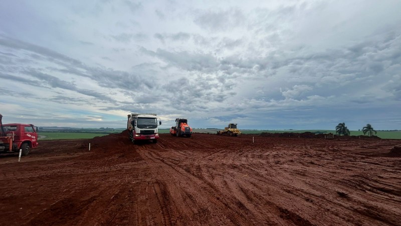 Canteiro de terraplenagem com máquinas pesadas operando sobre solo vermelho.