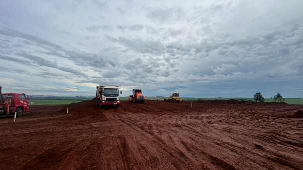 Canteiro de terraplenagem com máquinas pesadas operando sobre solo vermelho.