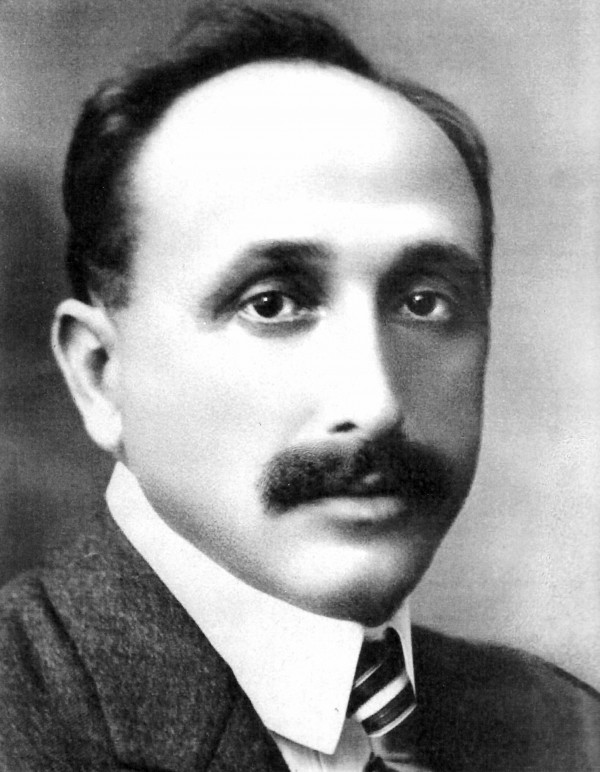 Foto em preto e branco de um homem branco de bigodes, vestindo terno e gravata.