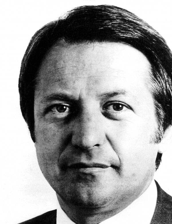 Retrato em preto e branco de um homem branco de cabelos escuros e vestindo terno.