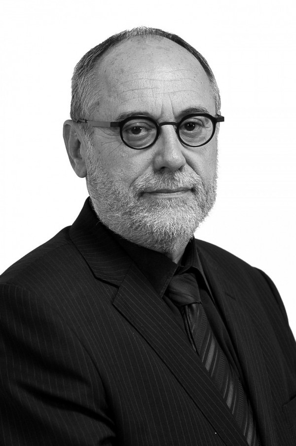 Retrato em preto e branco de um homem branco de barba branca, vestindo terno e gravata pretos e usando óculos.