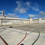 Na imagem, vê-se duas goleiras e uma cesta de basquete em uma quadra esportiva,