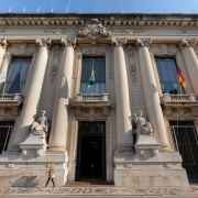 Foto de um palácio de dois pisos. Uma mulher caminha em frente a ele.