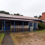 Foto do prédio da escola, de tijolo à vista. O tempo está chuvoso, com o pátio molhado.