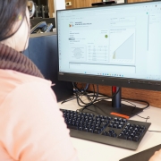Foto de uma mulher vestida de rosa e de cabelos pretos usando um computador. Na tela, aparece um gráfico crescente.